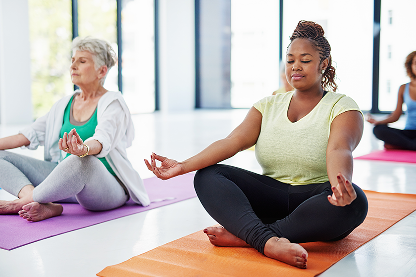 Elderly and diverse women practicing seated yoga meditation indoors to promote health and mindfulness