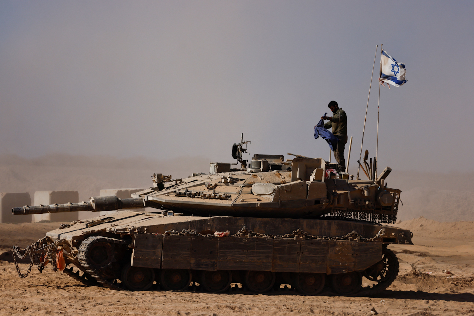 An Israeli Defense Forces tank with an Israeli flag stands in a desert environment during military operations