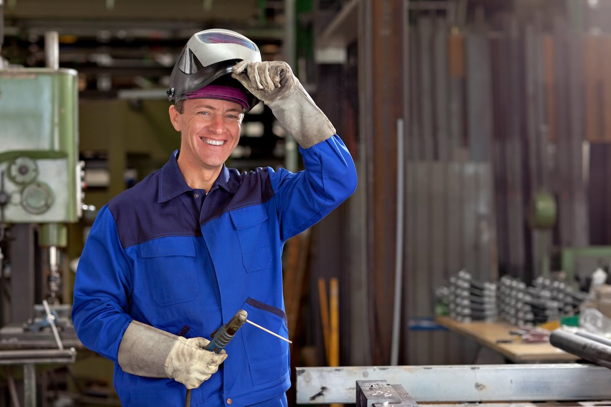 Professional welder in protective gear working in metal fabrication workshop