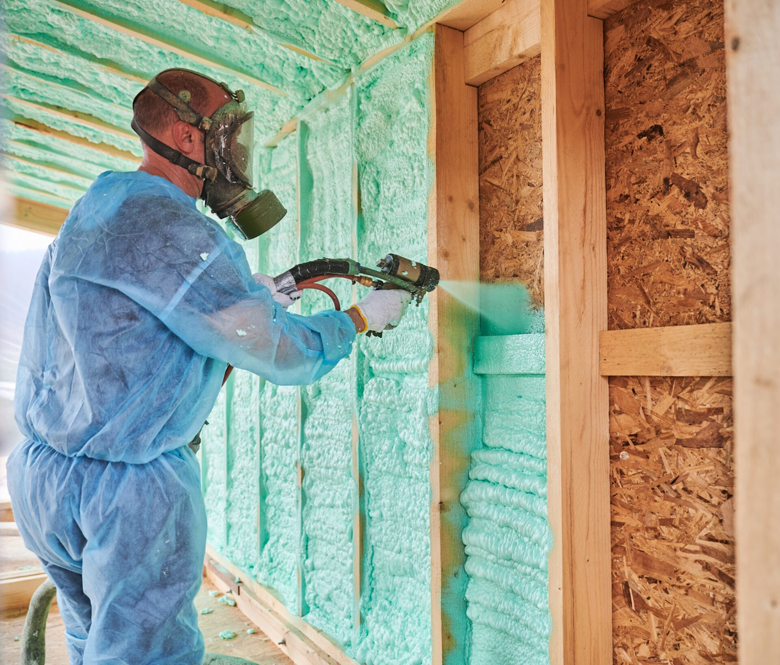 Worker applying spray foam insulation to building construction for thermal efficiency