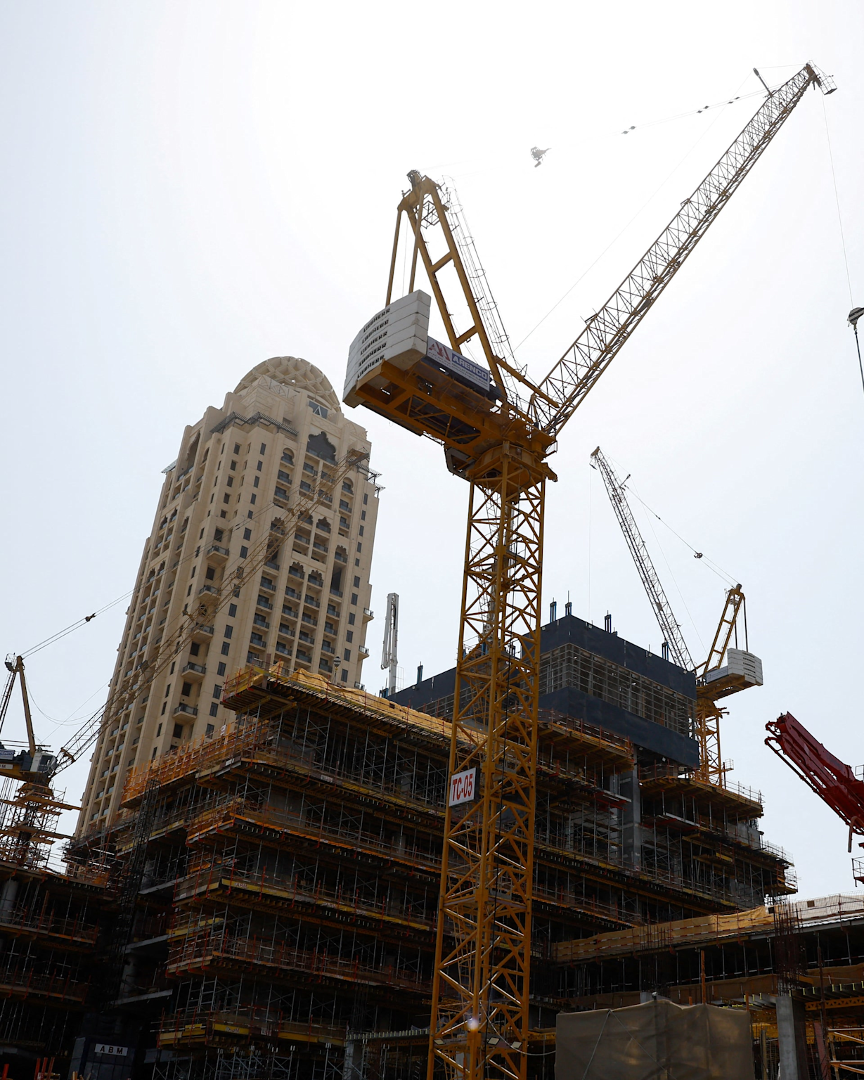 Construction cranes at a multi-story urban development site with a completed high-rise in the background