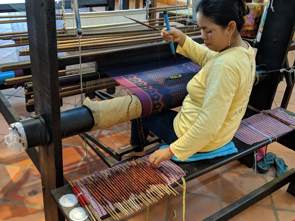 A Cambodian artisan weaving traditional Khmer silk fabric on a handloom, showcasing the rich cultural heritage and craftsmanship