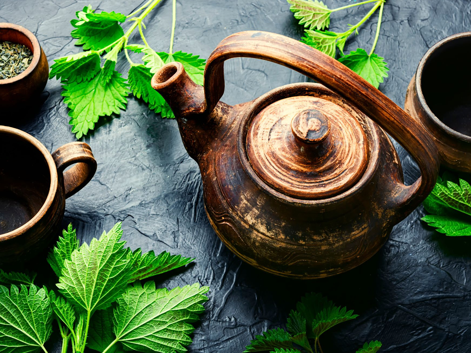 Rustic ceramic teapot with fresh nettle leaves and cups showcasing traditional herbal tea preparation