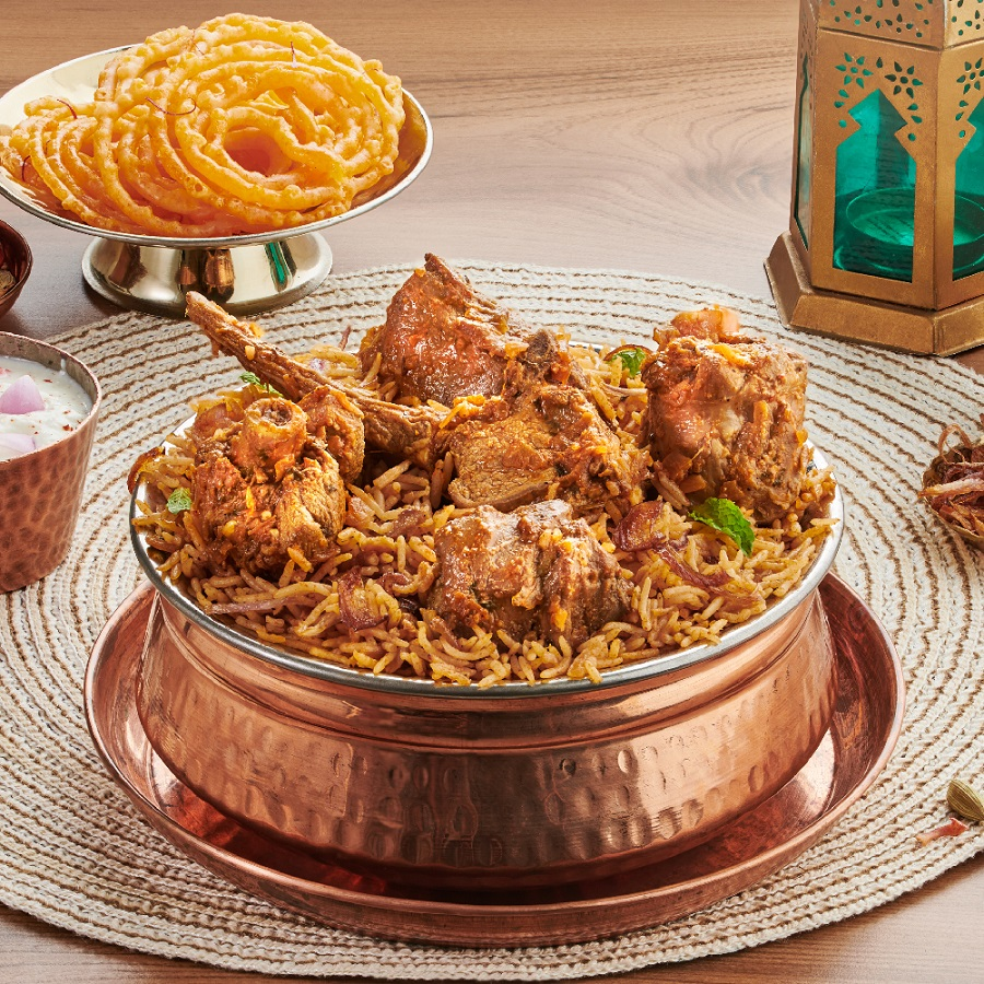Traditional Hyderabadi Mutton Biryani served in a copper bowl with raita and jalebi, showcasing authentic Indian cuisine presentation