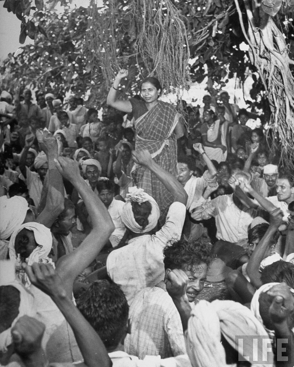 A historic protest scene showing a woman leader addressing and inspiring a crowd of demonstrators with raised fists under a banyan tree