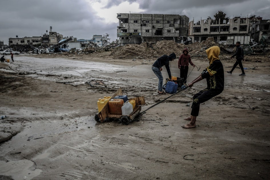 Children in Gaza pull a cart with water containers amidst destroyed buildings and wartorn surroundings highlighting humanitarian crisis