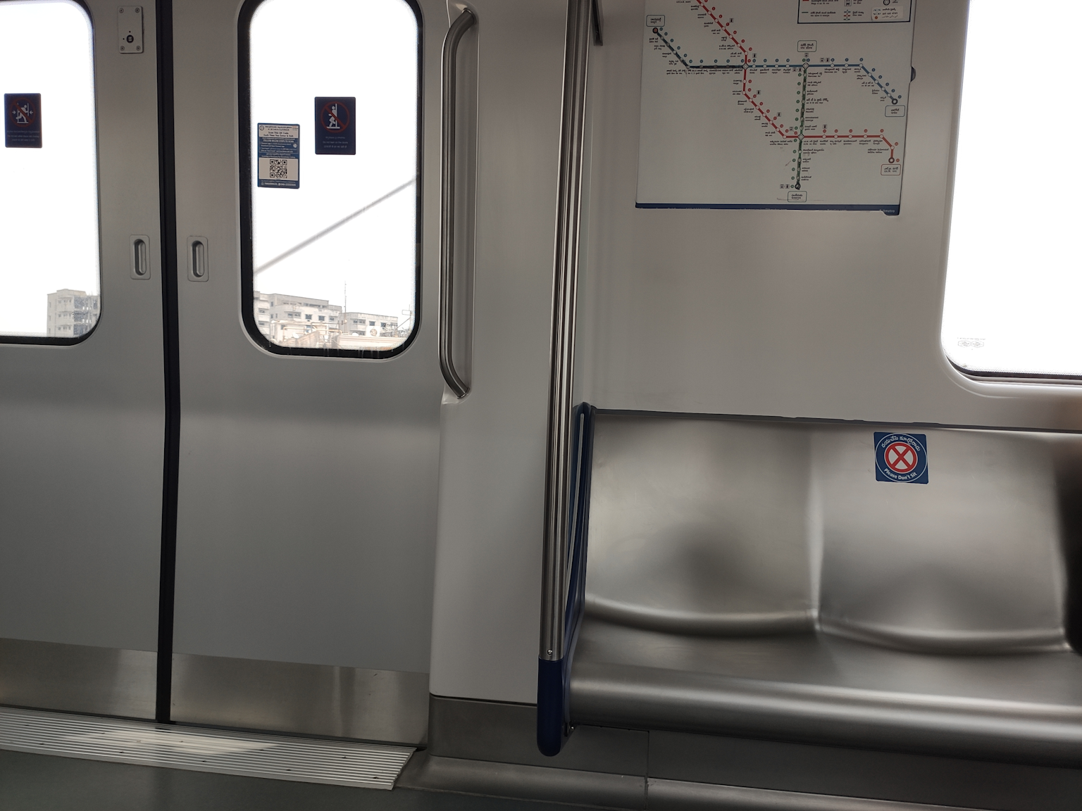 Interior view of an air-conditioned Hyderabad Metro Rail coach with folding seats, handrails, and a route map for commuter guidance