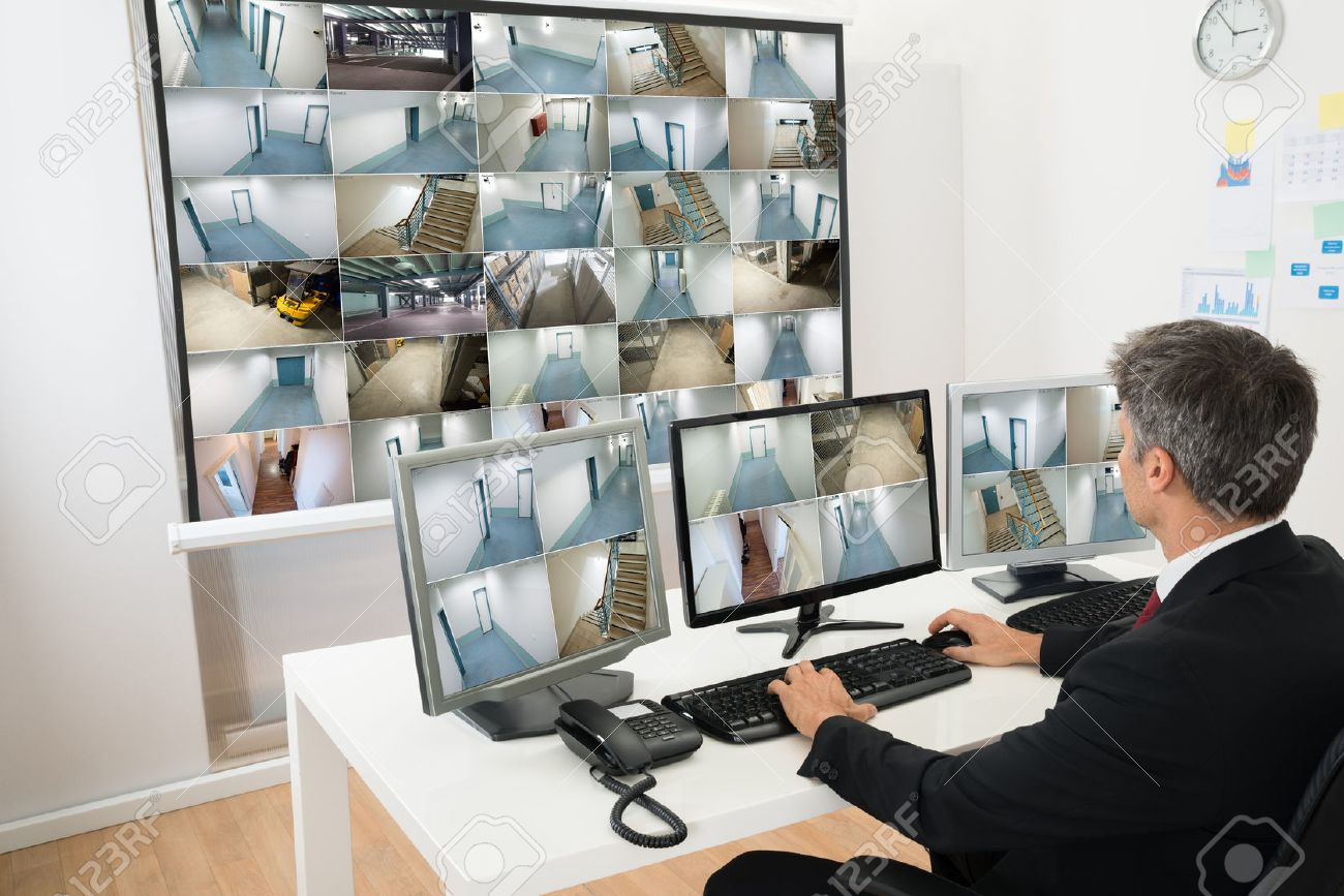 Man monitoring multiple CCTV camera feeds in a surveillance control room.