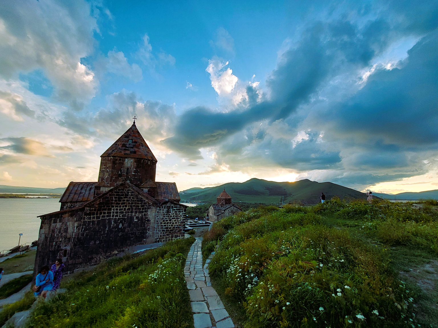 An ancient stone church overlooking the scenic Lake Sevan in Armenia at sunset, surrounded by lush greenery and mountains
