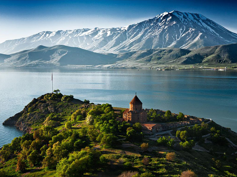 Lake Sevan, Armenia, featuring a historic church on a green peninsula surrounded by serene water and majestic mountains