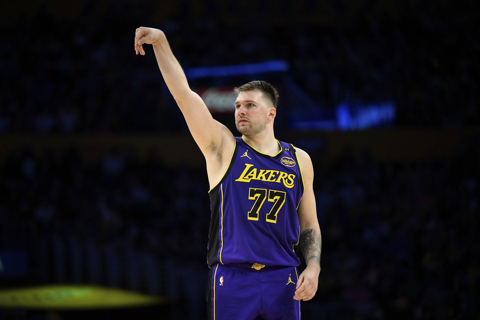 Luka Doncic wearing a Los Angeles Lakers jersey, raising his arm in a shooting gesture during a game.