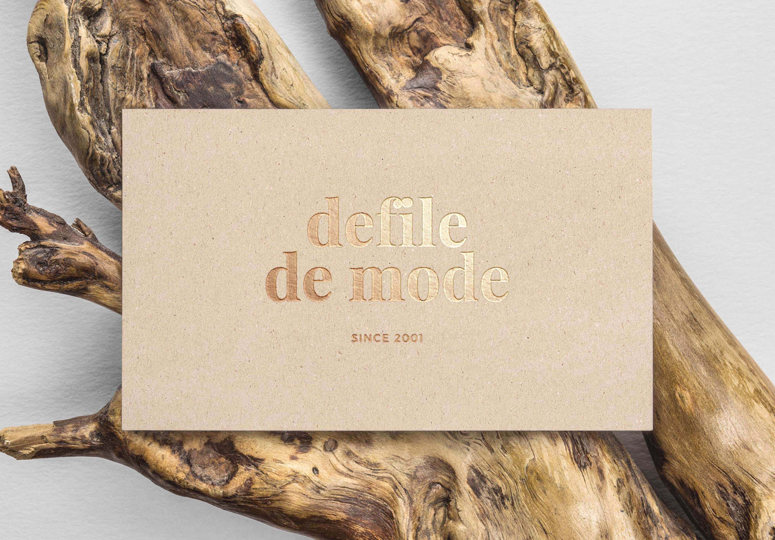 A kraft paper business card with gold embossed text on a natural wood background demonstrating texture and embossing techniques.