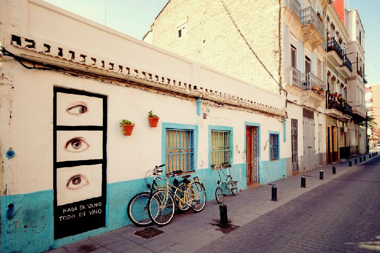 Traditional Street Scene In El Cabanyal, Valencia, Showcasing Local Art And Bicycles Along Colorful Rustic Buildings