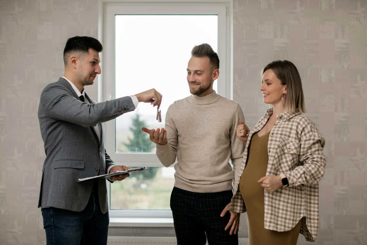 A person handing over keys to a couple during a new home handover inside a well-lit room
