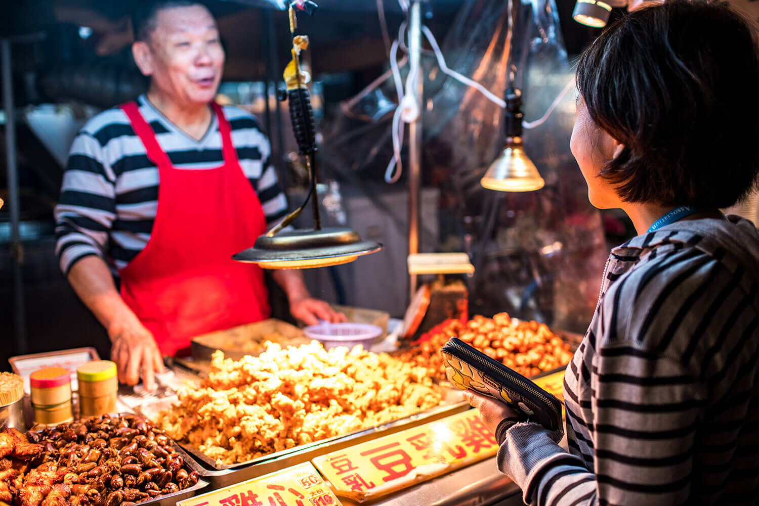 Taipei night market street food vendor serving a customer, showcasing popular fried snacks under warm lighting