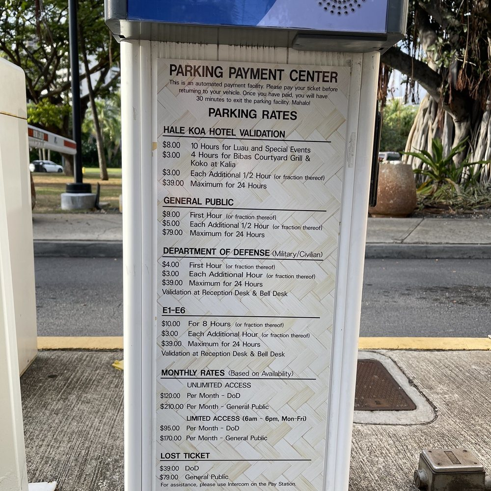 Parking payment rates sign showing fees for Hale Koa Hotel, general public, military personnel, and monthly plans in a Hawaii tourist area