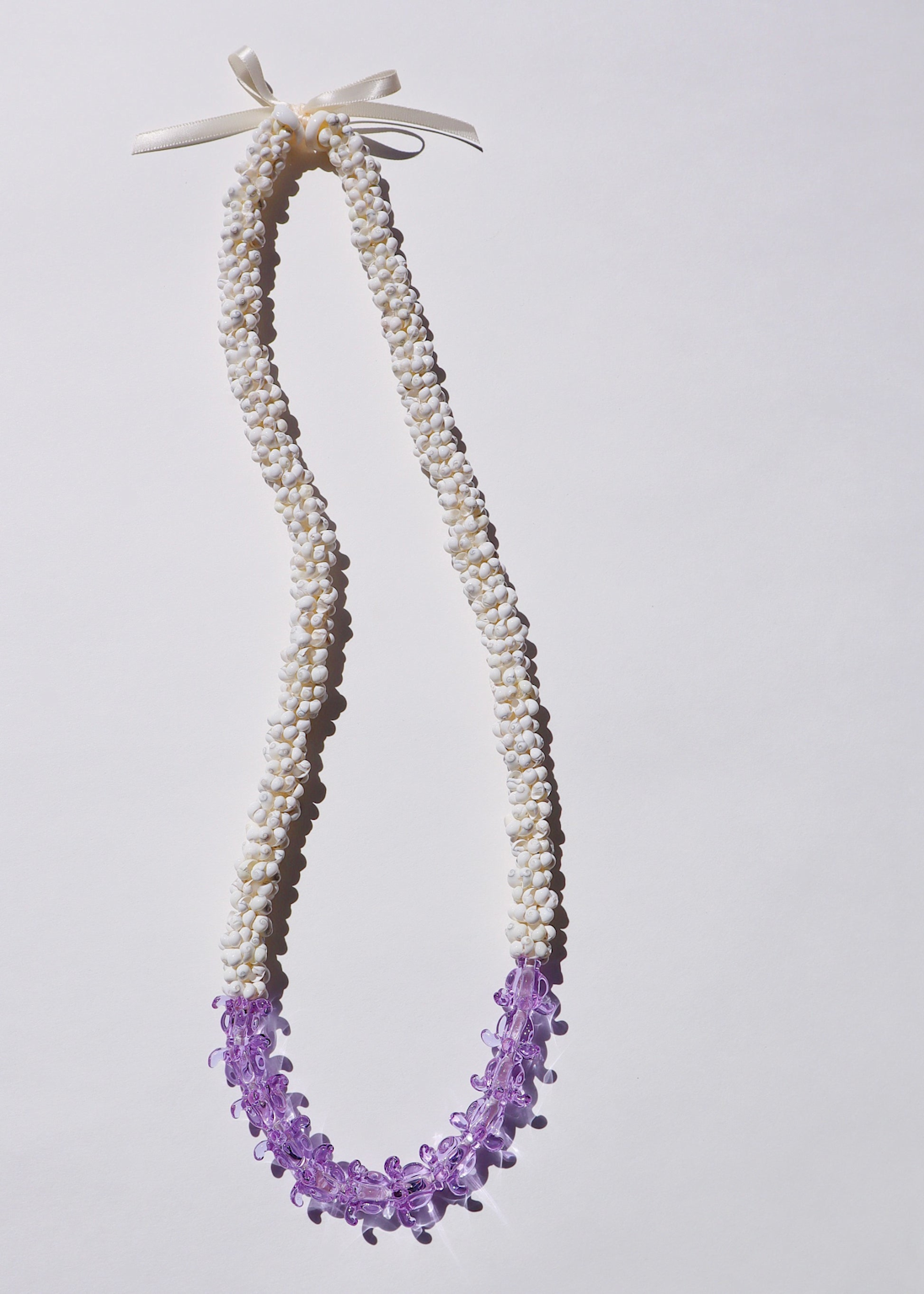 Traditional Hawaiian shell lei with white shells and purple glass flowers often sold as tourist souvenirs