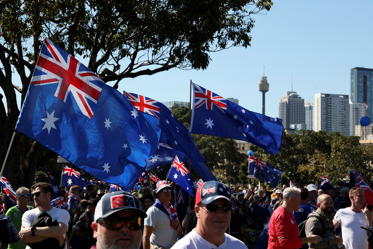 Crowd waving Australian flags during a 2025 Sydney anti-immigration rally with city skyline in background