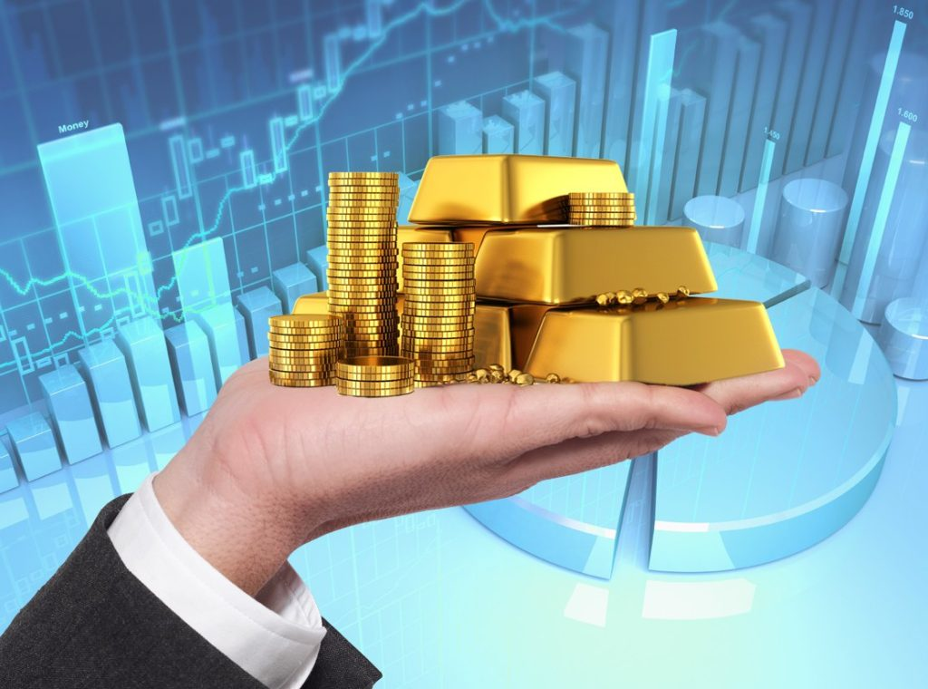 Hand holding gold bars and coins with financial market charts in the background illustrating gold investment and value