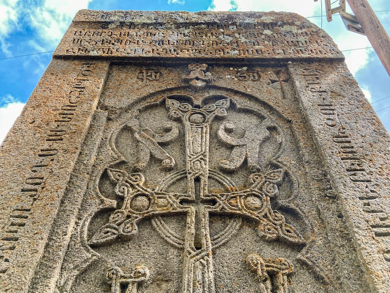 An intricately carved Armenian khachkar stone cross showcasing detailed Christian motifs and Armenian inscriptions against a bright sky
