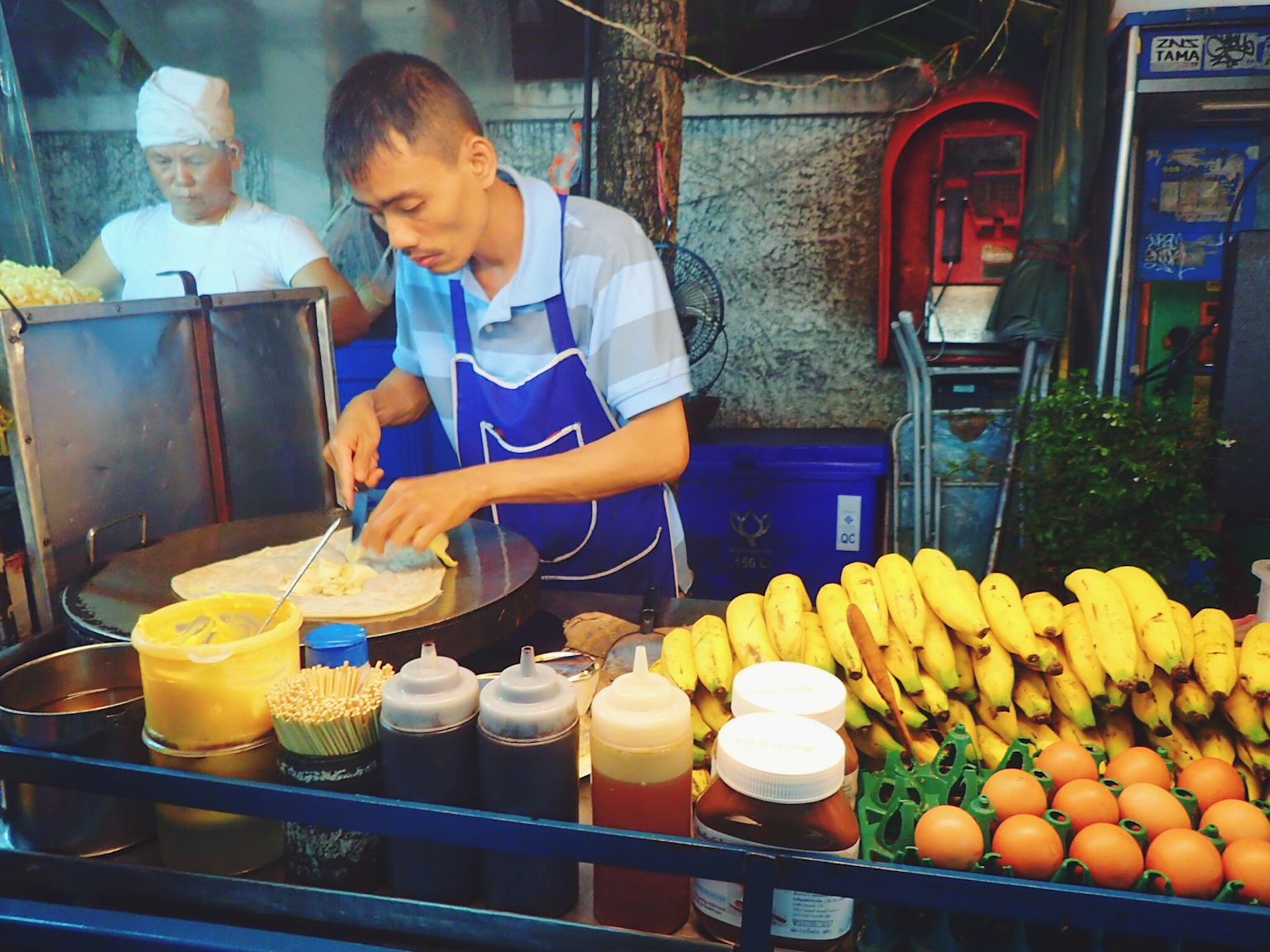 Street food vendor preparing affordable local dishes with fresh ingredients in a Southeast Asian market