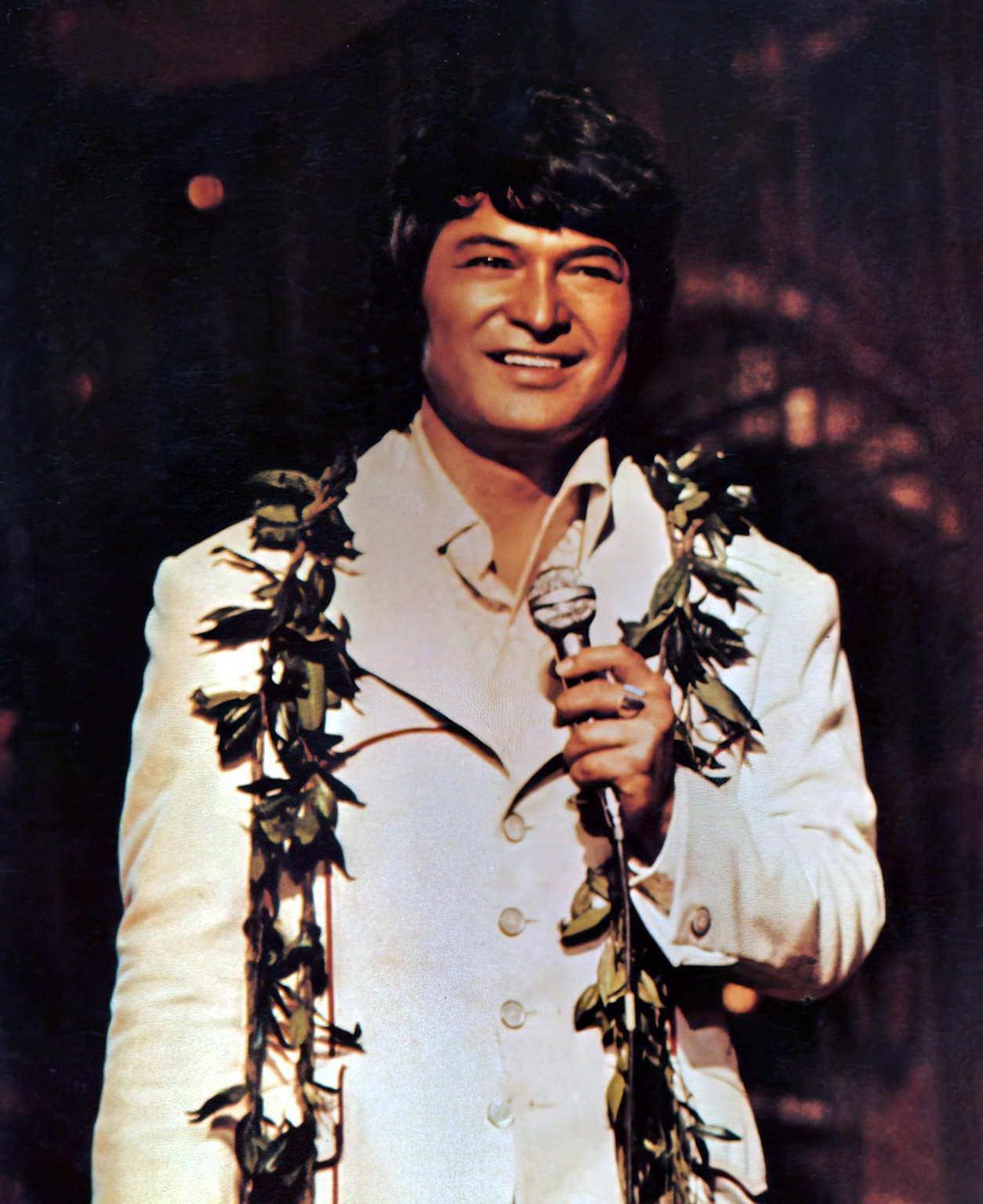 Don Ho performing in a white jacket with a traditional Hawaiian lei, embodying the spirit of Hawaiian music