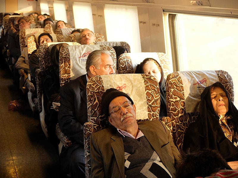 Interior view of a passenger train in Iran showing modern seating and branding related to a railway cooperation project