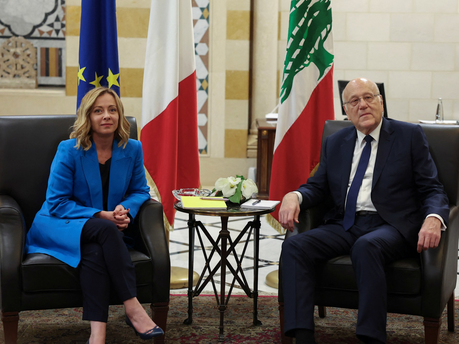Diplomatic meeting between Italian and Lebanese representatives with flags of the EU, Italy, and Lebanon in the background
