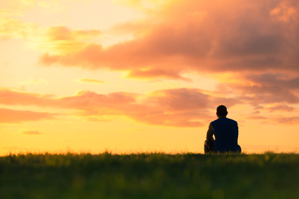 A person sits contemplatively during a sunset, symbolizing peaceful reflection and acceptance of uncertainty.