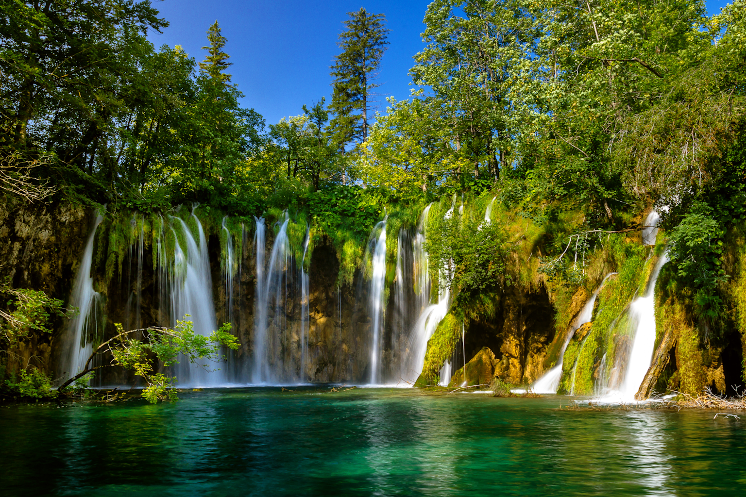 Cascading waterfalls in the lush, enchanted forests of Plitvice Lakes National Park, Croatia, resembling a real-life fantasy landscape