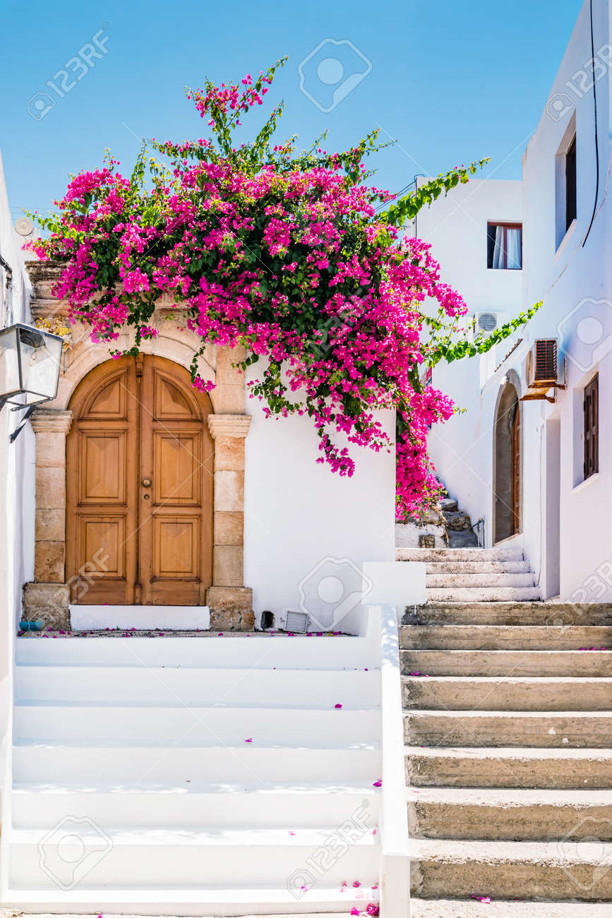 Traditional whitewashed buildings with vibrant bougainvillea flowers in a picturesque Greek village, ideal for romantic solo travel
