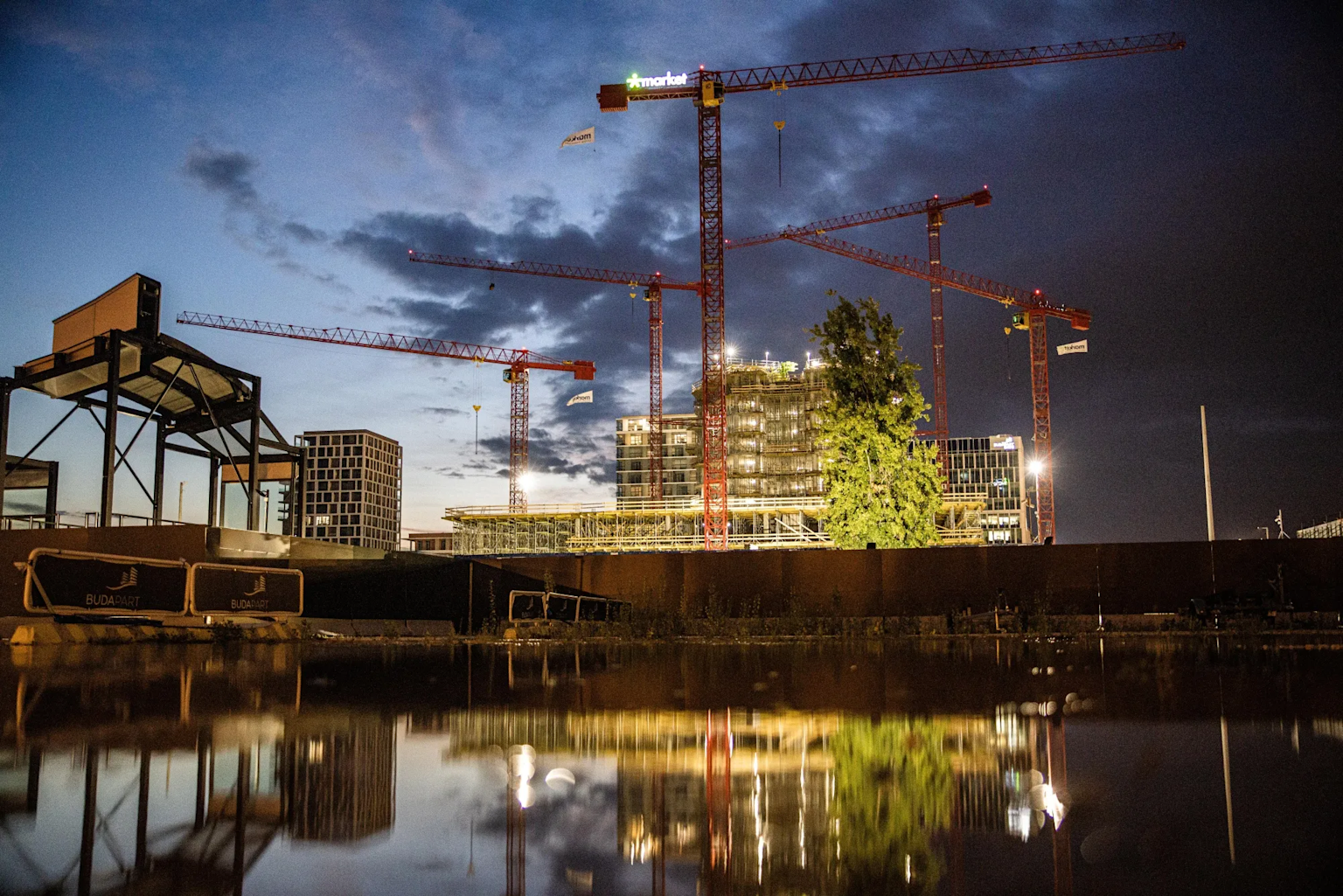 Construction site with cranes in an Eastern European city at dusk reflecting in a water body