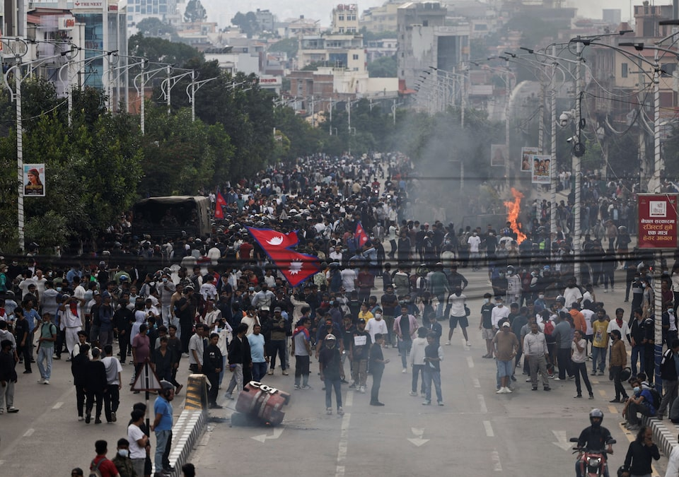 Large crowds of protesters in Kathmandu, Nepal, waving national flags amid smoke and fire during Gen Z social media ban demonstrations in September 2025
