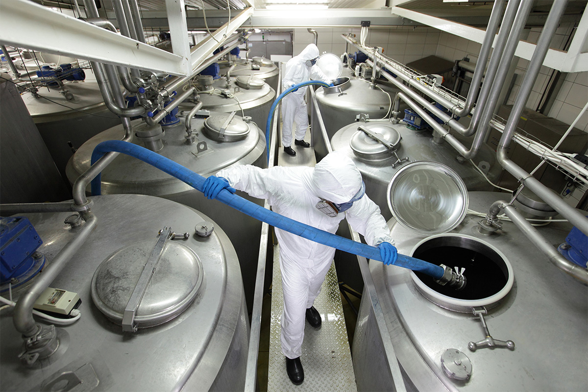 Workers wearing protective suits handling large stainless steel tanks in a food processing facility, illustrating industrial odour control environment