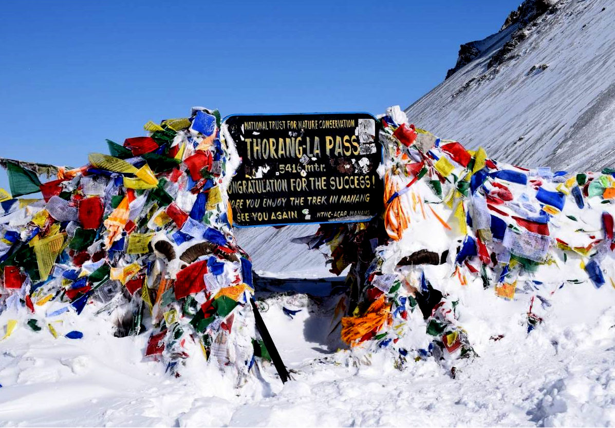 Thorong-La Pass signboard at 5416 meters marked with colorful prayer flags in the snowy Himalayas, symbolizing trekking success and cultural depth in Nepal