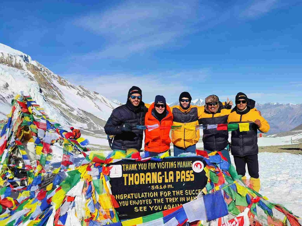 Trekkers celebrate reaching the summit of Thorong La Pass (5,416m) on the Annapurna Circuit, Nepal, surrounded by prayer flags and snow-clad peaks