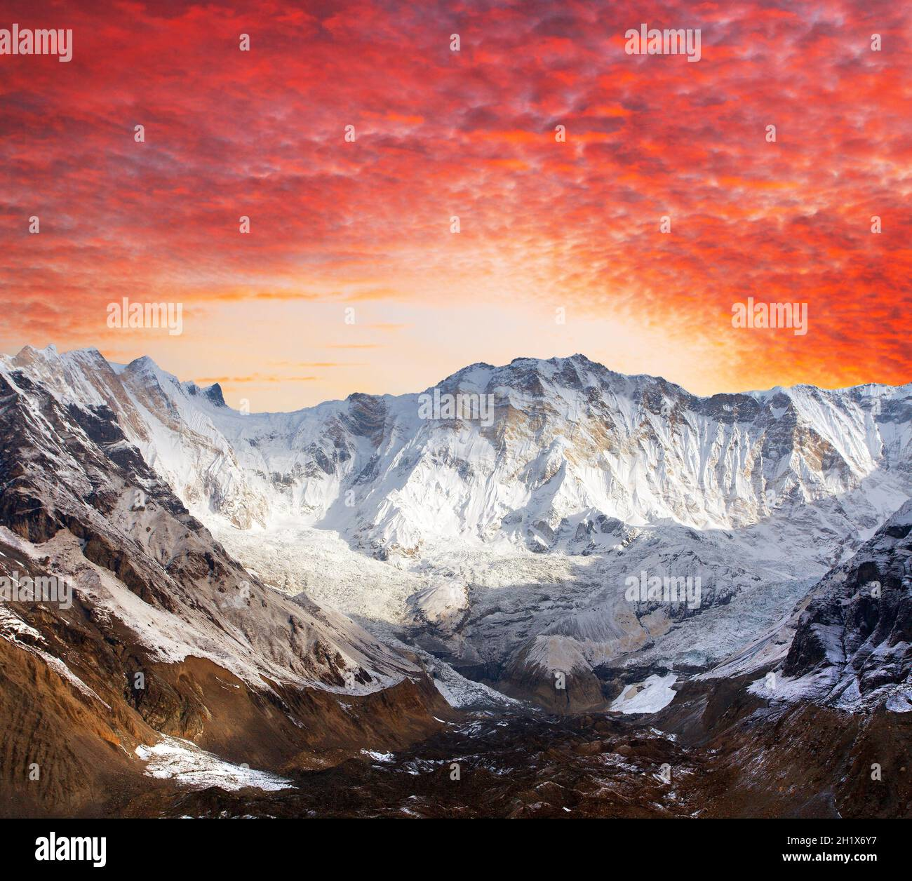 Sunrise illuminates the snow-covered peaks of the Annapurna mountain range in a vivid red and orange sky panorama