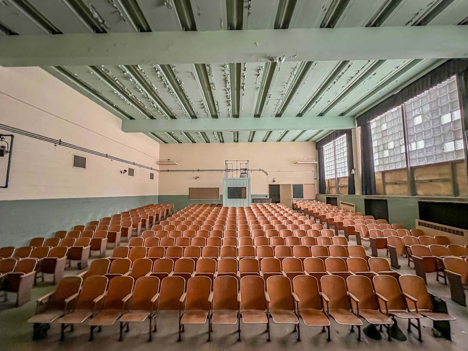 Empty university lecture hall with rows of wooden seats and large windows