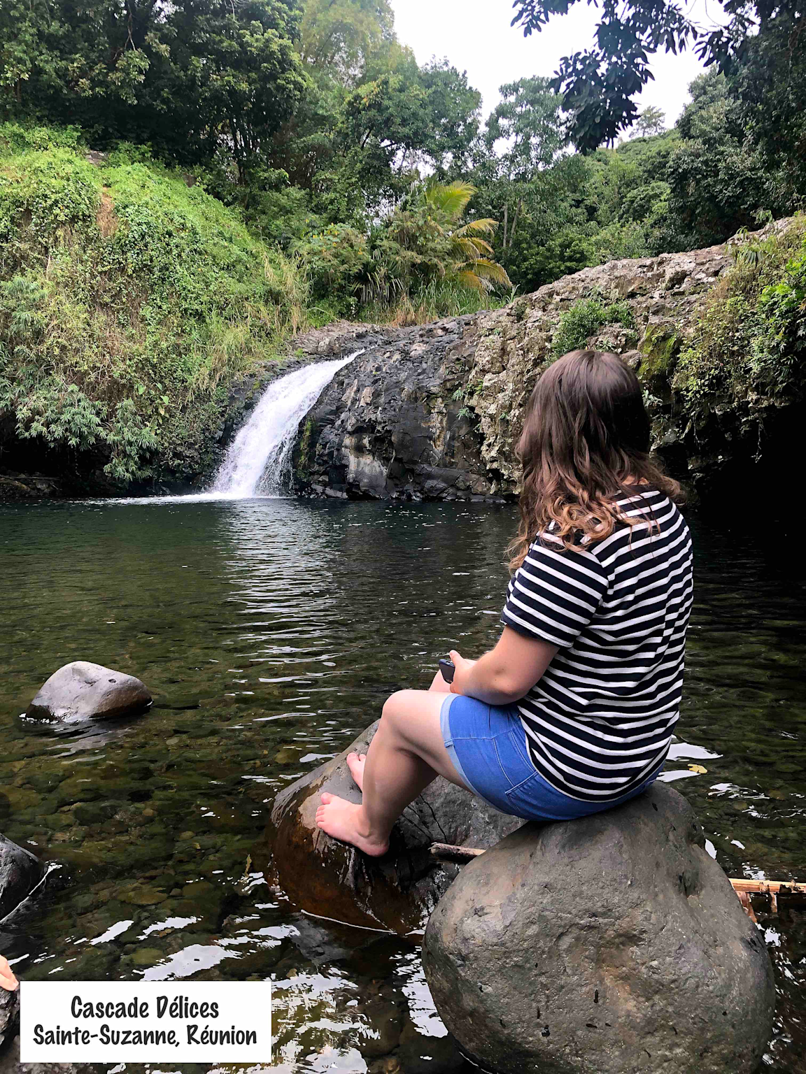 A woman enjoys the tranquil Cascade Délices waterfall and natural pool in Sainte-Suzanne, Réunion Island, an offbeat family-friendly hiking destination