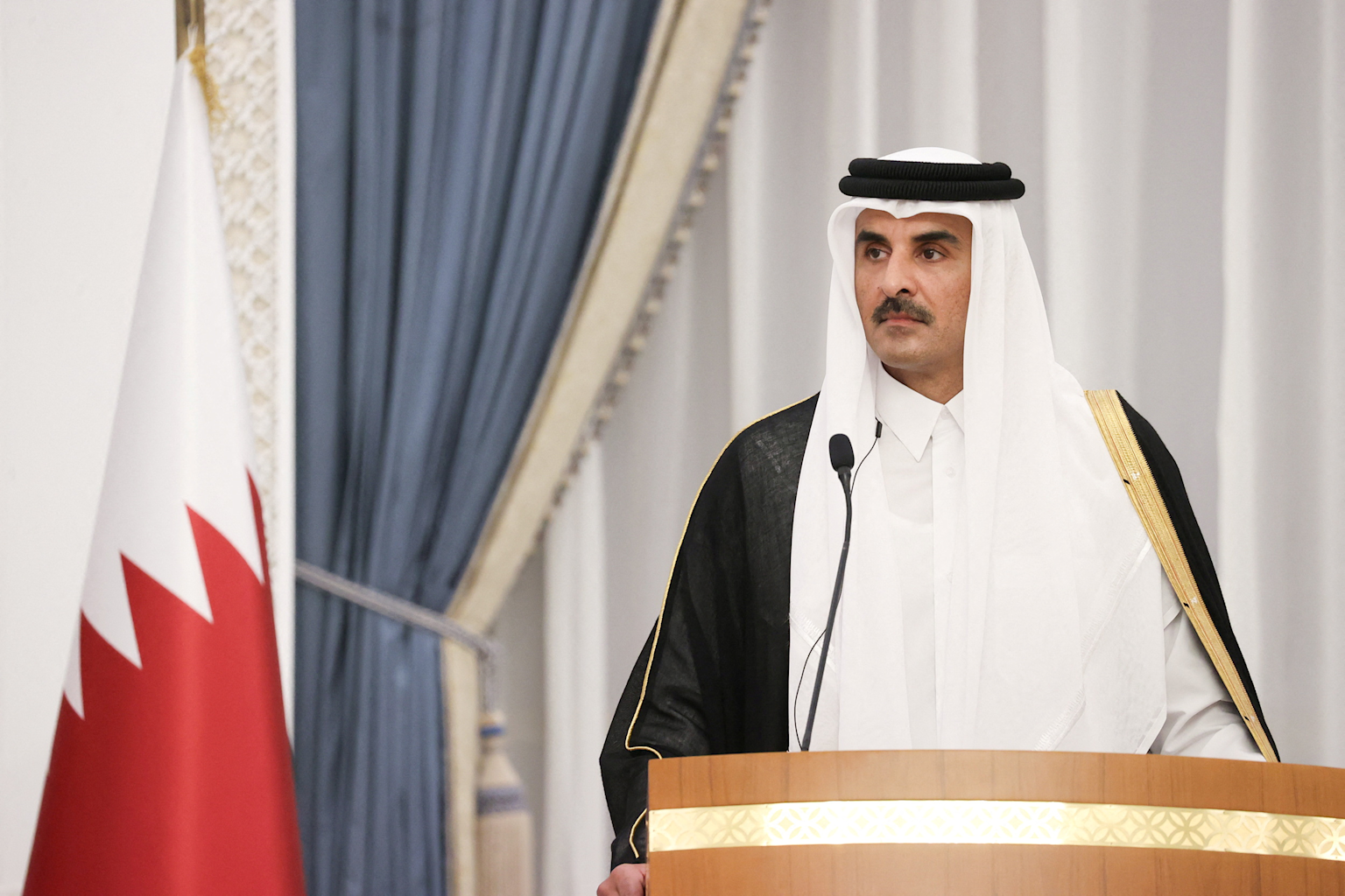 Qatar's emir delivers a formal speech at a podium with the national flag during an official event