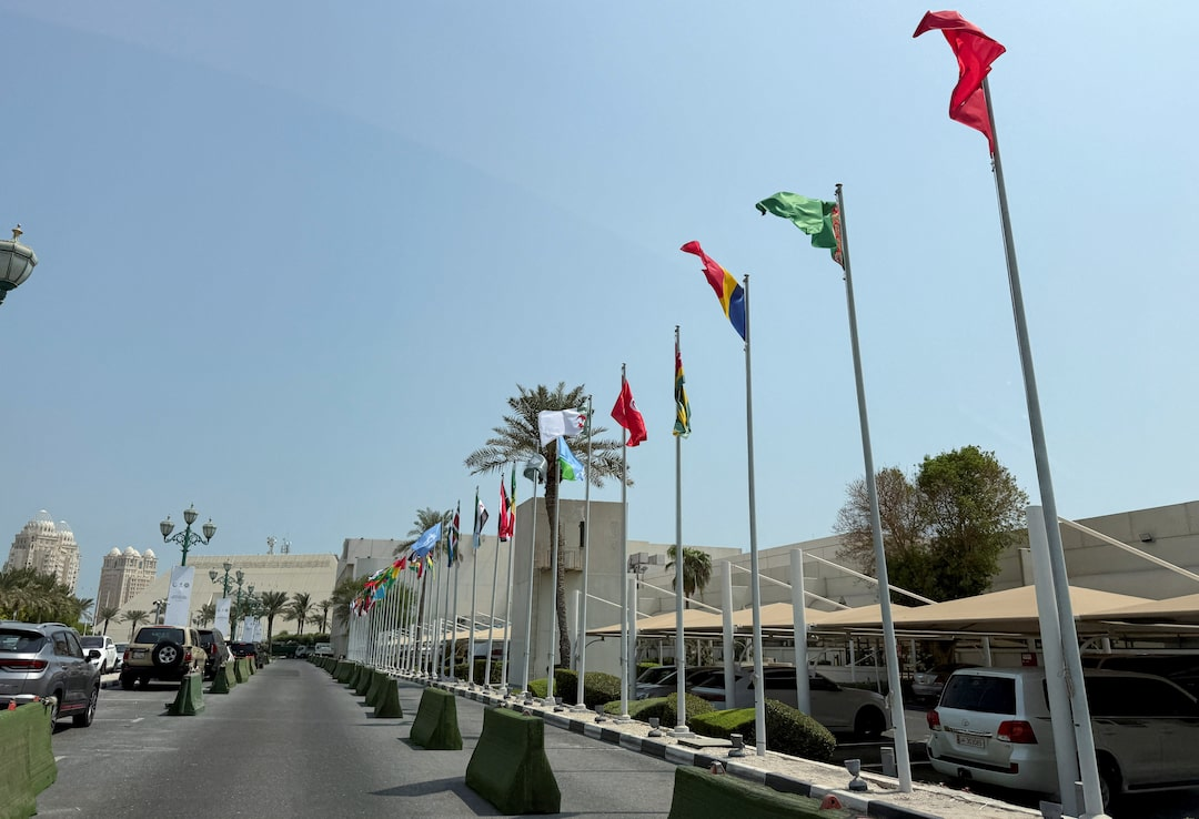 Flags of various nations including Qatar displayed at a Middle Eastern summit venue under clear skies, symbolizing international diplomatic engagement