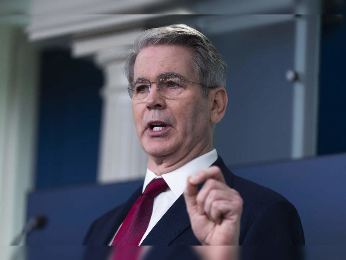 A senior government official in a formal suit gestures while speaking in an official setting