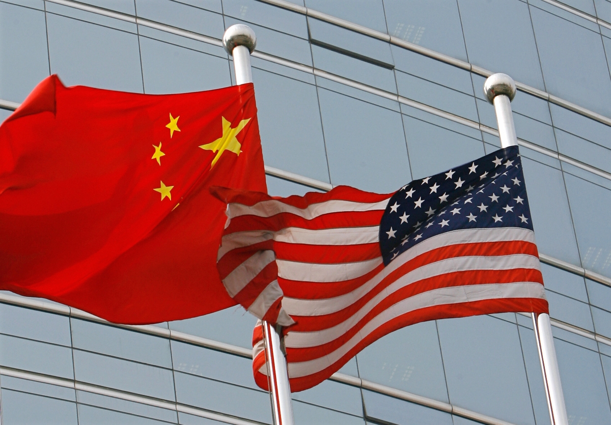 Flags of China and the United States fluttering side by side against a modern building, symbolizing USChina diplomatic relations