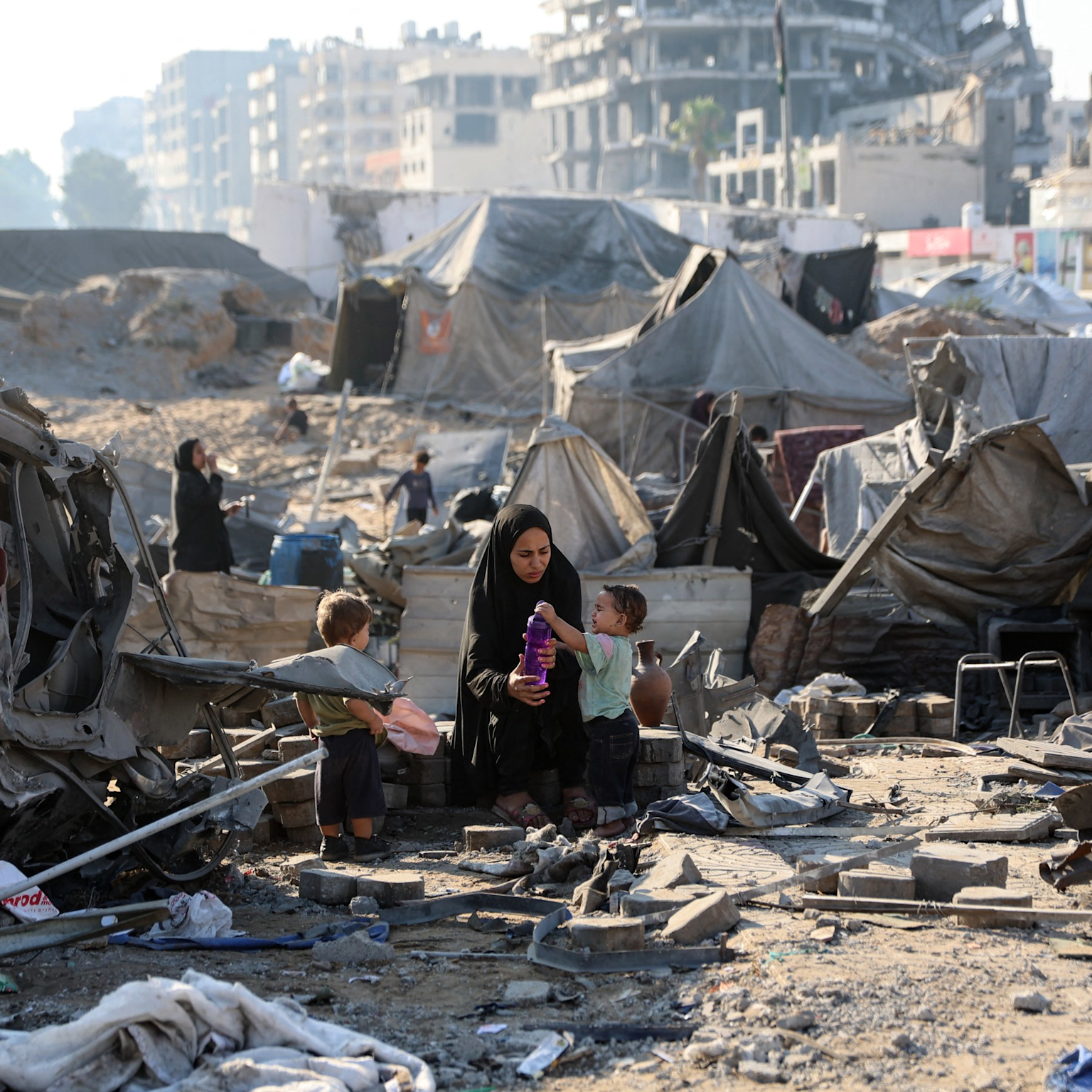 A displaced woman and children amidst rubble and makeshift tents in wardamaged Gaza City following heavy bombing and ground invasion
