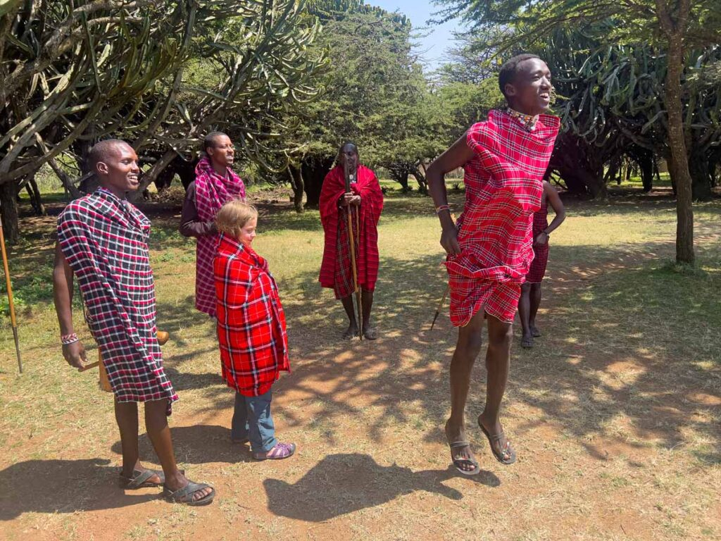 Children and adults enjoying a traditional Maasai cultural experience in a Kenyan village setting, highlighting family-friendly cultural immersion