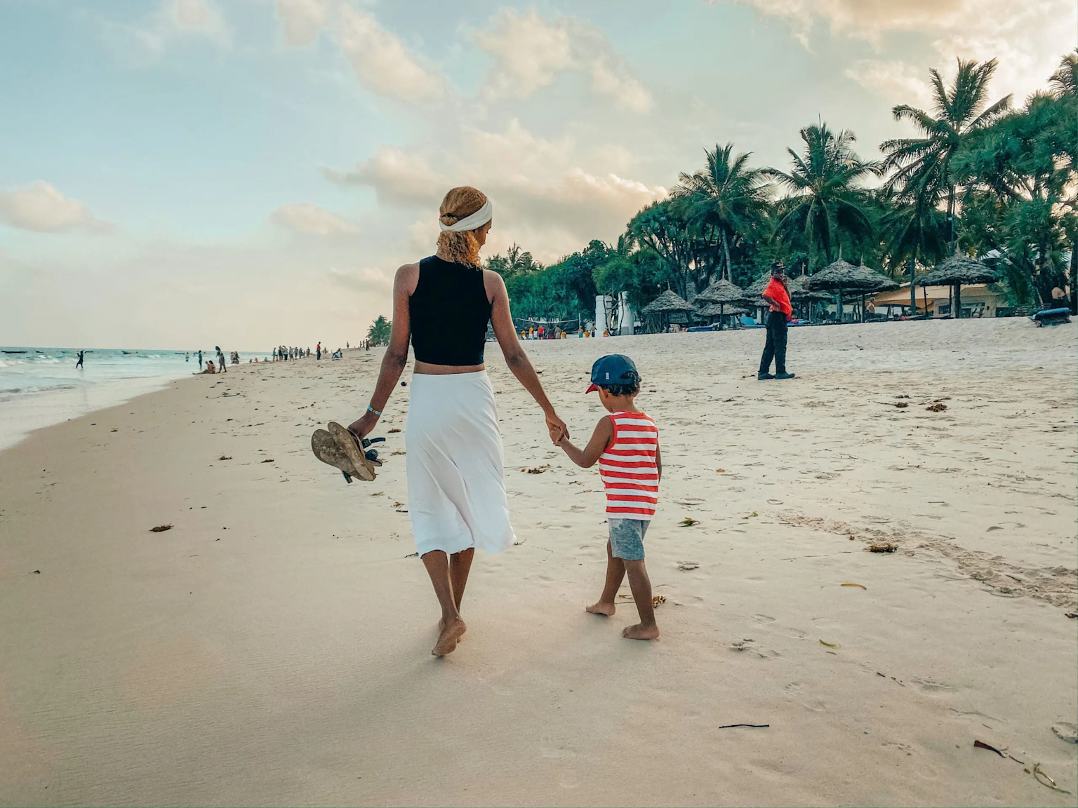 A mother and child walking hand in hand along the peaceful Diani Beach, Kenya, a perfect setting for family relaxation and connection by the Indian Ocean