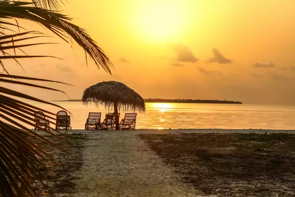 Sunset tranquility at a secluded tropical beach with palm-fringed shores and cozy lounge chairs under a straw umbrella