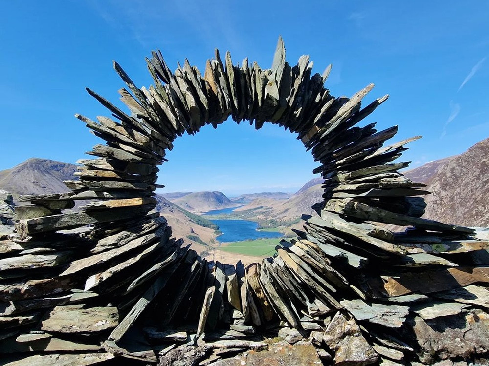 Circular stone sculpture framing a mountainous landscape, exemplifying land art that conveys deep time messaging through natural stone patterns
