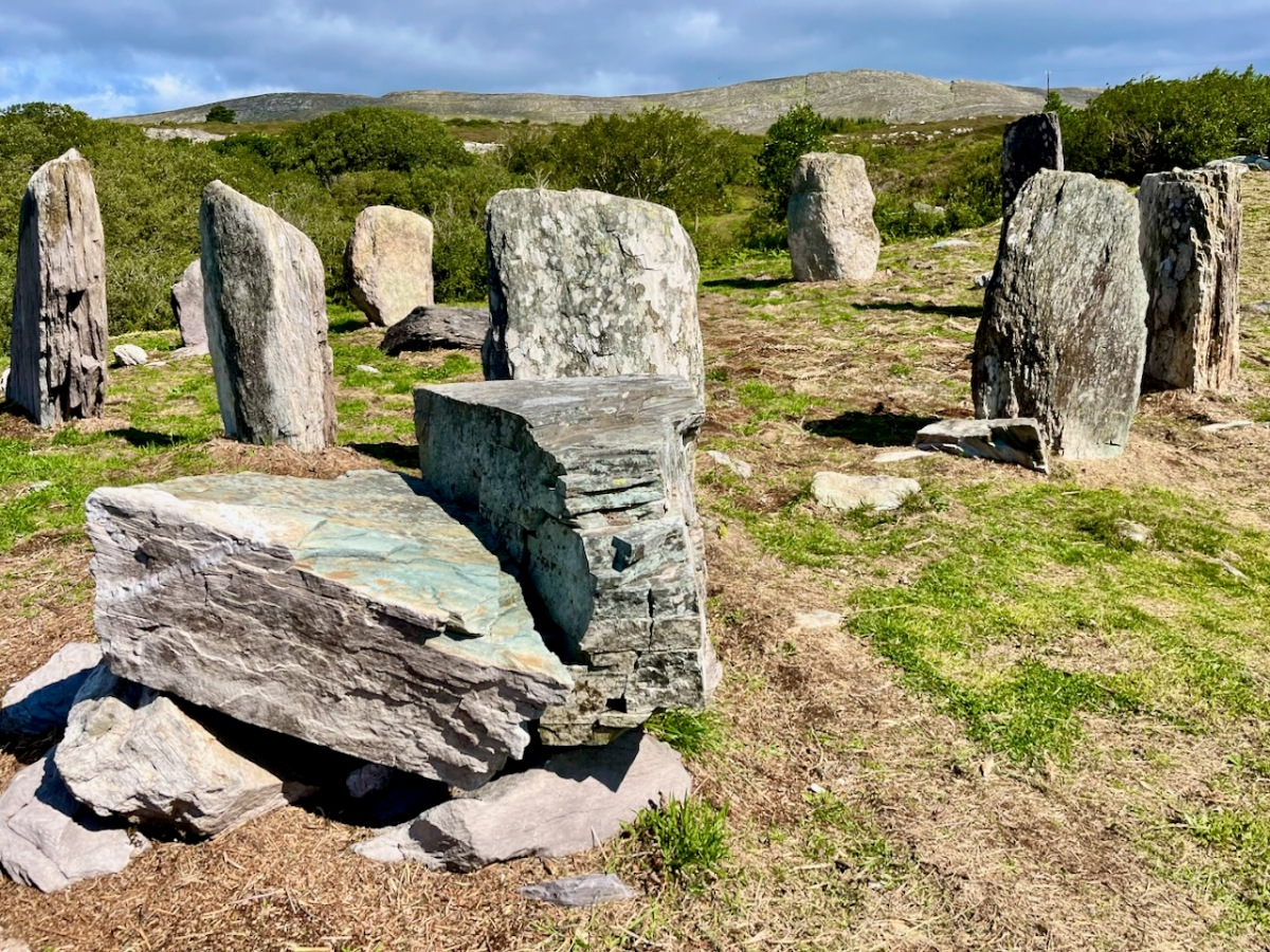 Stone circle with large, partly embedded stones arranged in a prehistoric pattern on grassy terrain