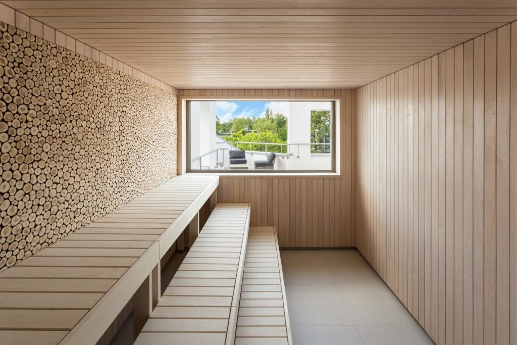 Modern spa sauna room with juniper wood décor and natural light from a large window overlooking a tranquil outdoor terrace in Estonia